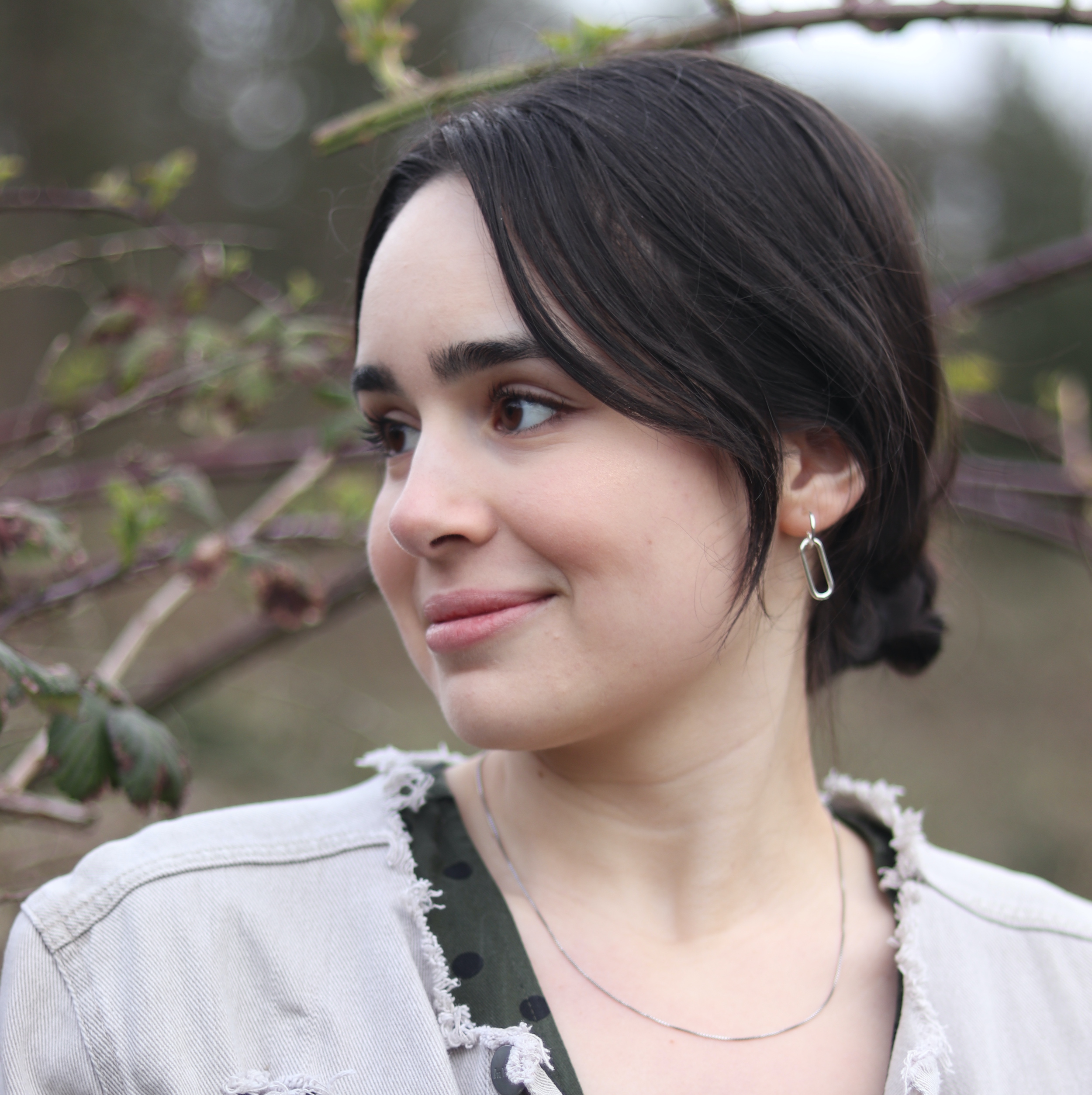 Demetra smiling and looking over her shoulder in front of a tree. 