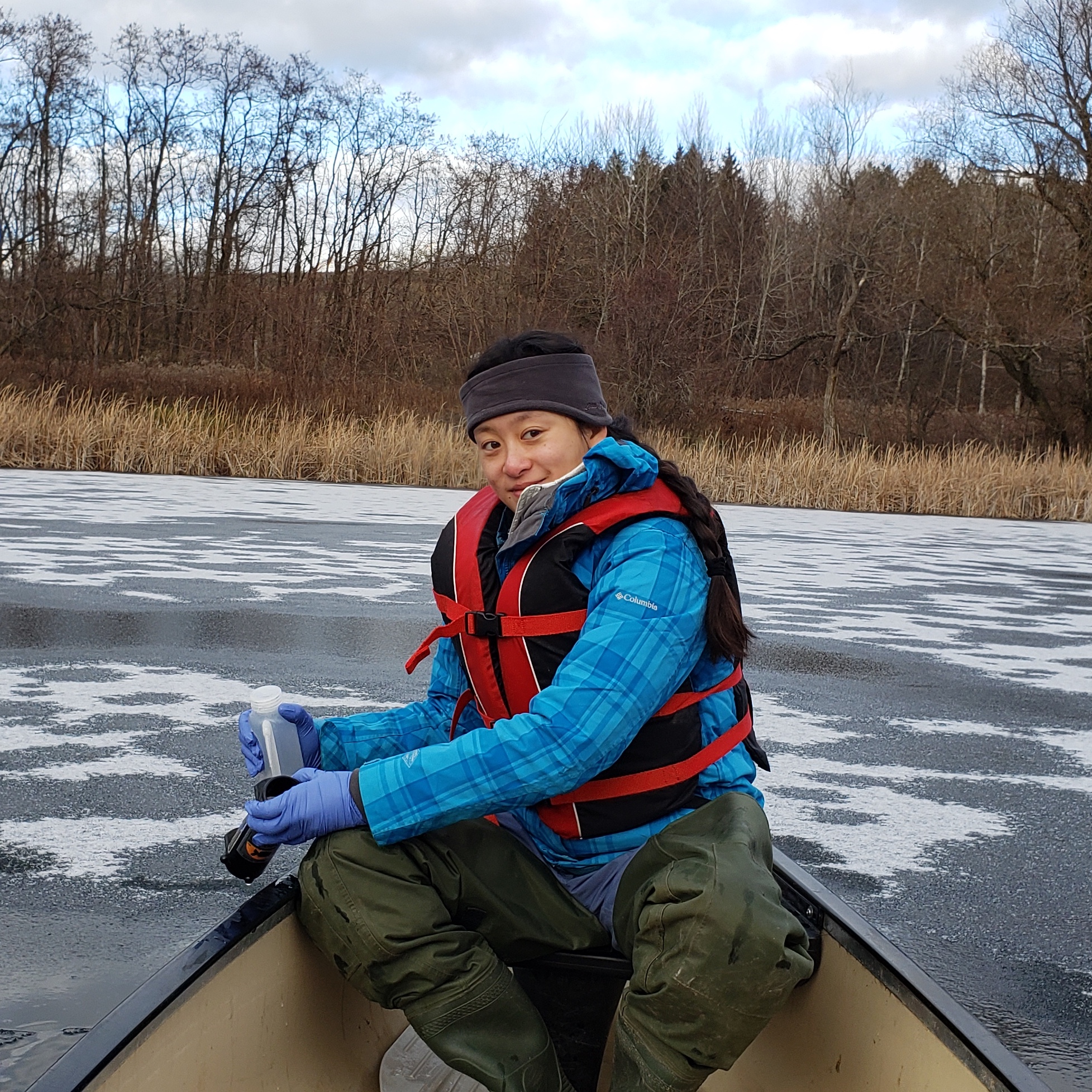 Shi Shu smiling and sitting in a boat in an icy river with a paddle in her hand. 