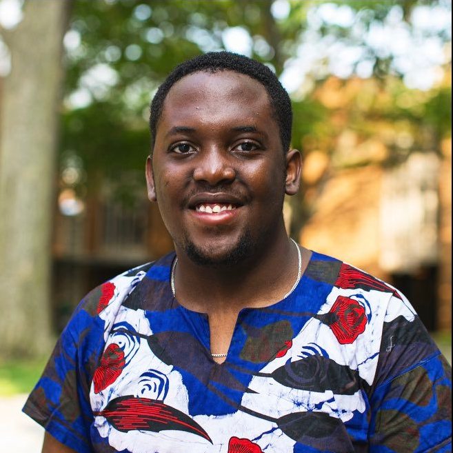 Moboluwajidide smiling in blue and red graphic T-shirt in front of some trees. 