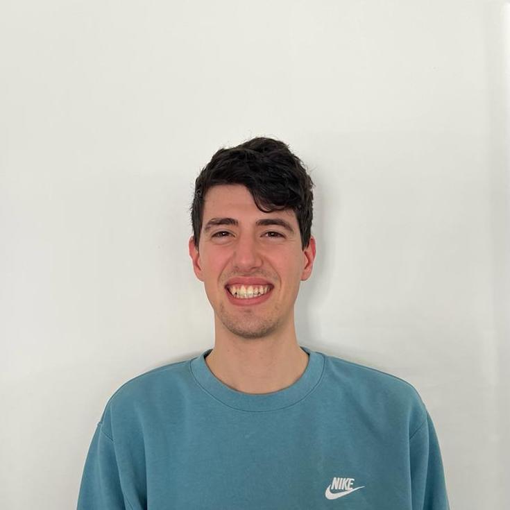 Alex smiling in a blue sweater in front of a white wall.