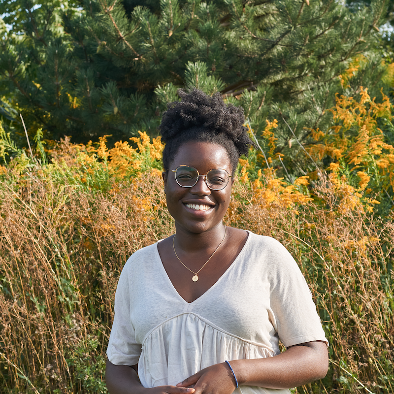 Alexandra smiling and standing in front of field of yellow flowers. 