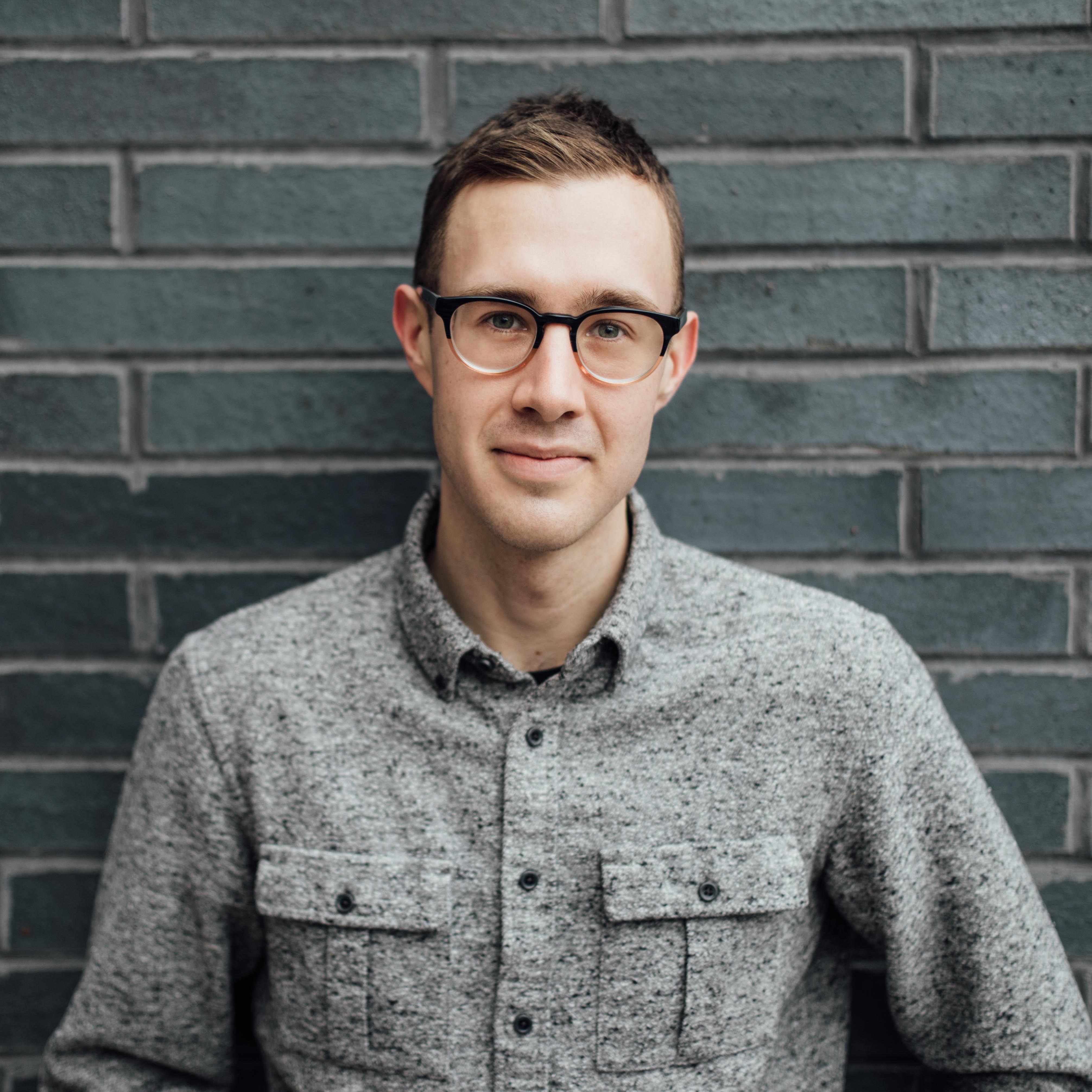 Andrew smiling in front of a brick wall. 