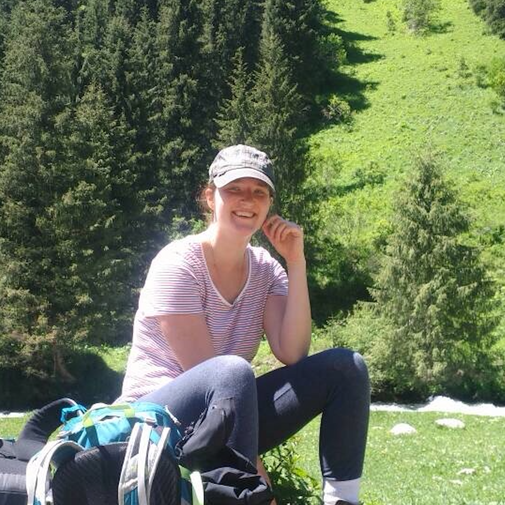 Ariella sitting and smiling in front of forest. 