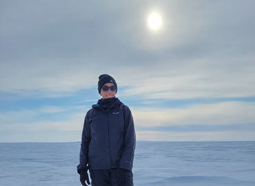 Brianna stands in an arctic setting with snow, wearing winter gear, the sun shining above