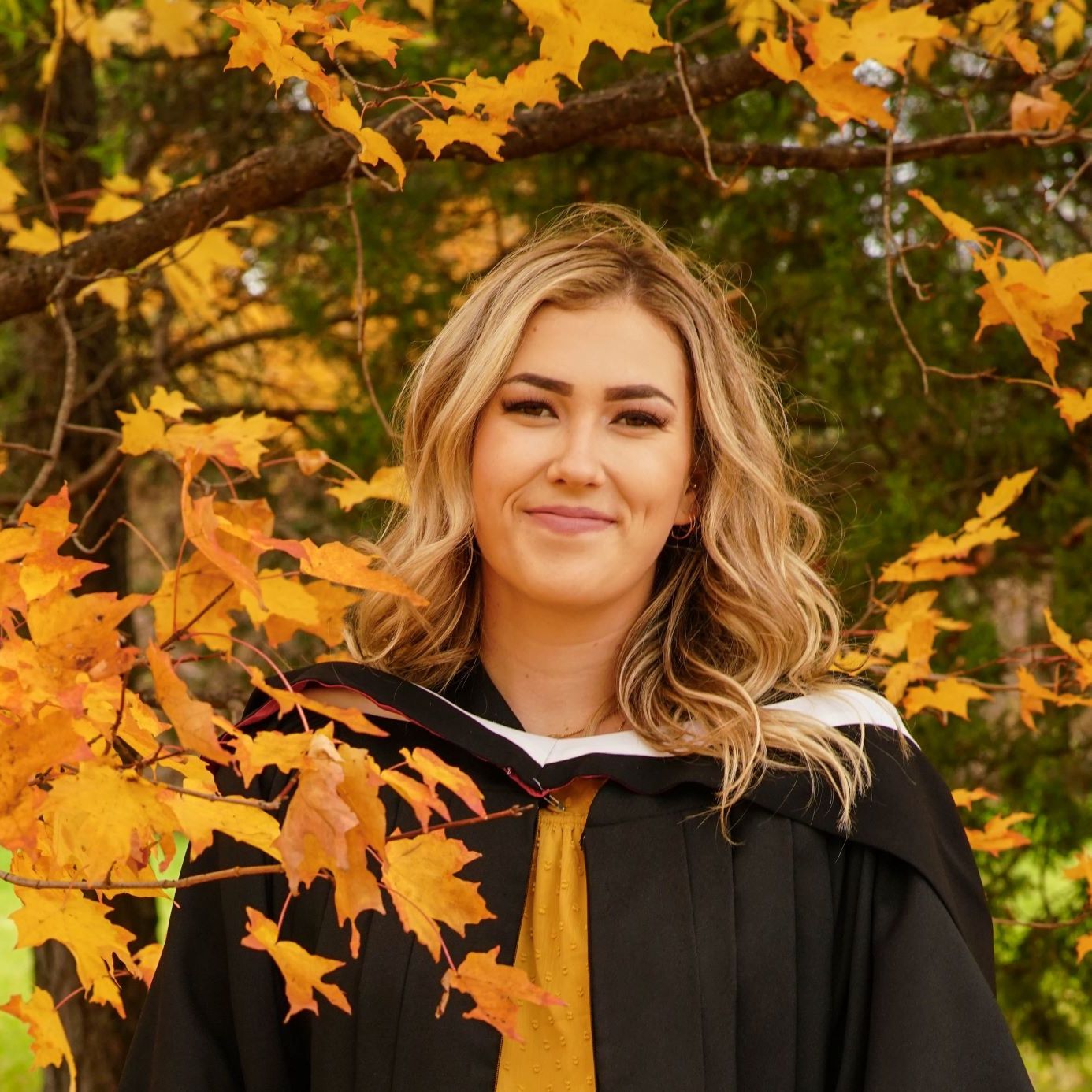 Brooke smiling in front of yellow leaves and trees. 