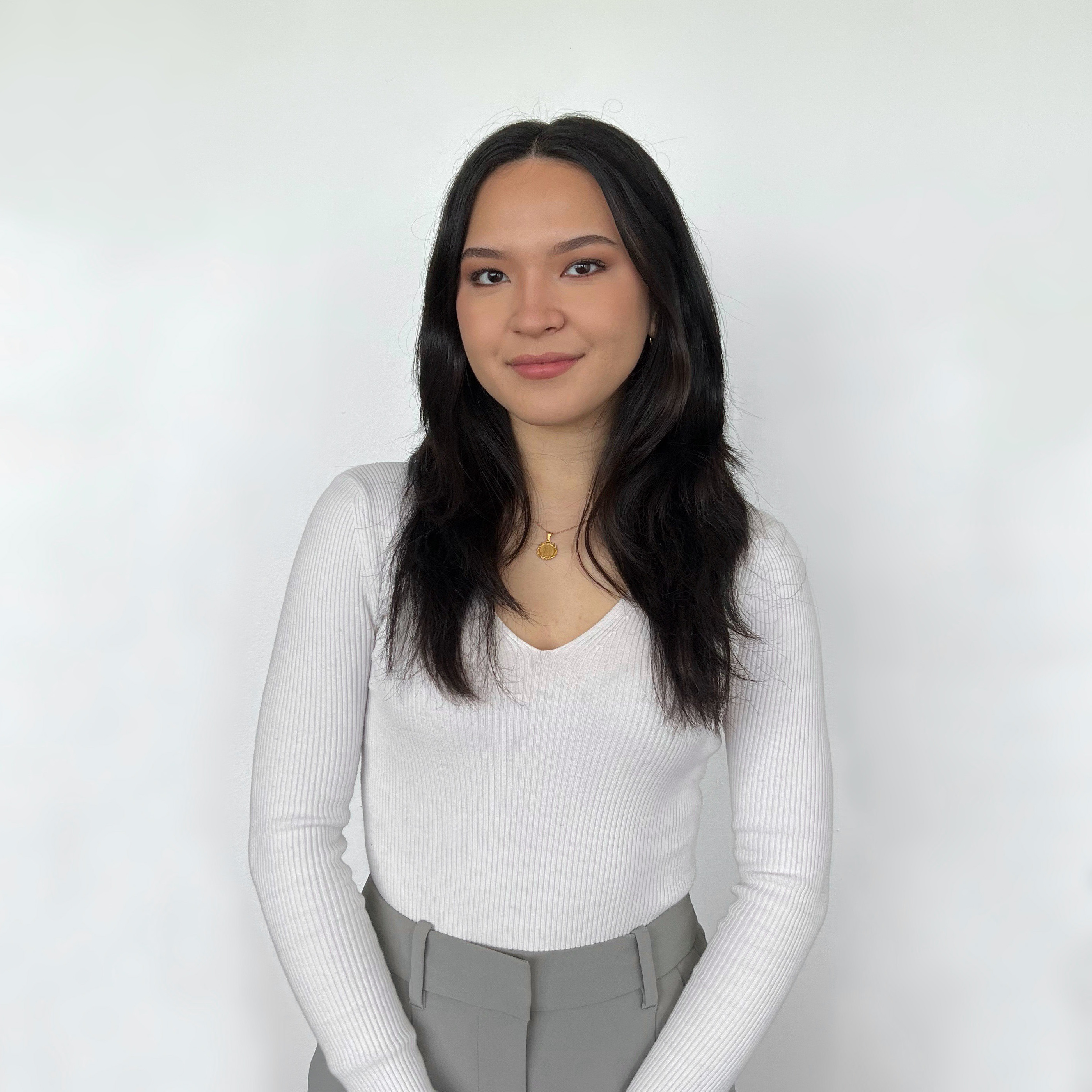 Sonia standing and smiling in front of a white wall. 