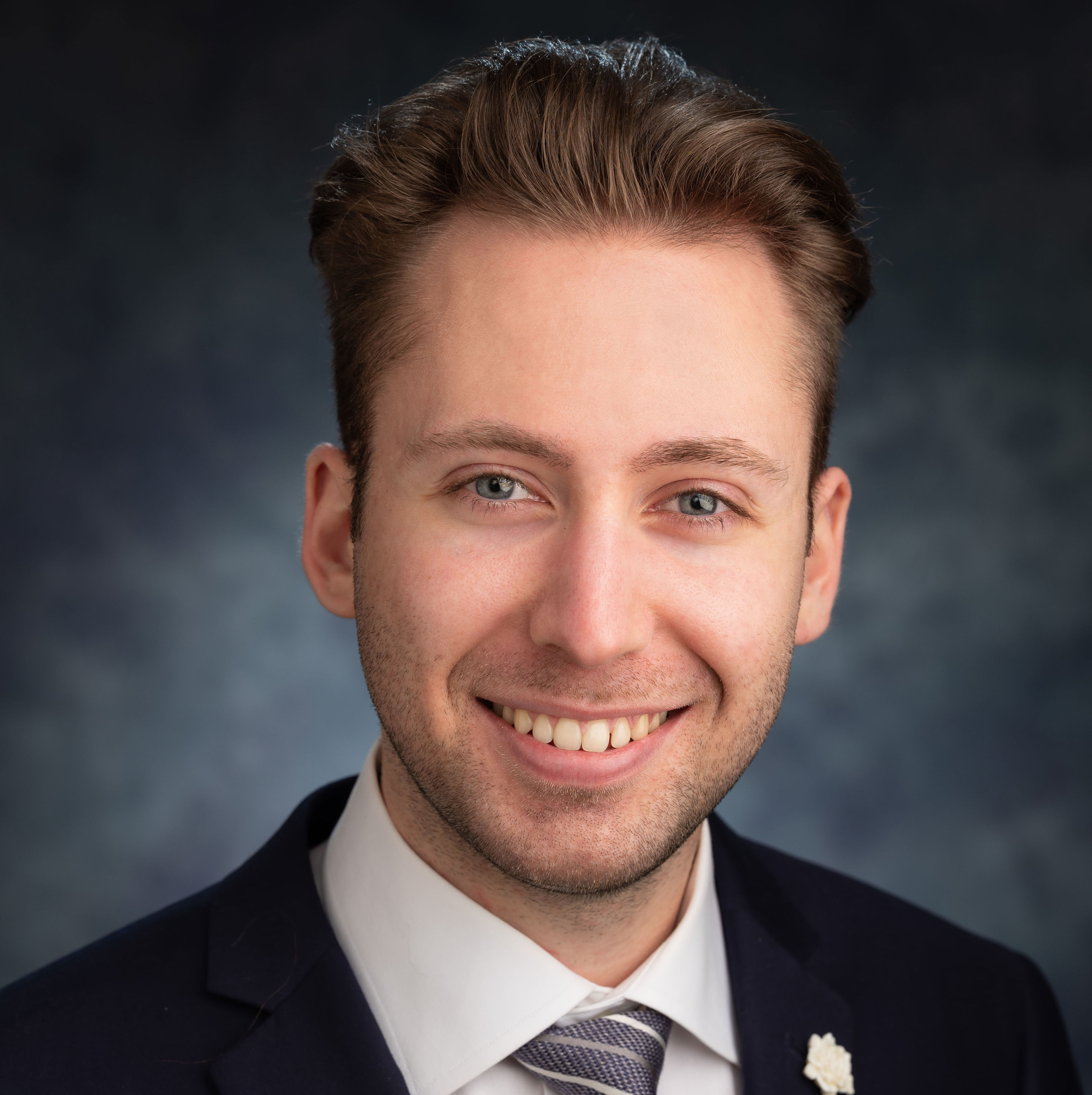 Daniel smiling in front of a blue background. 