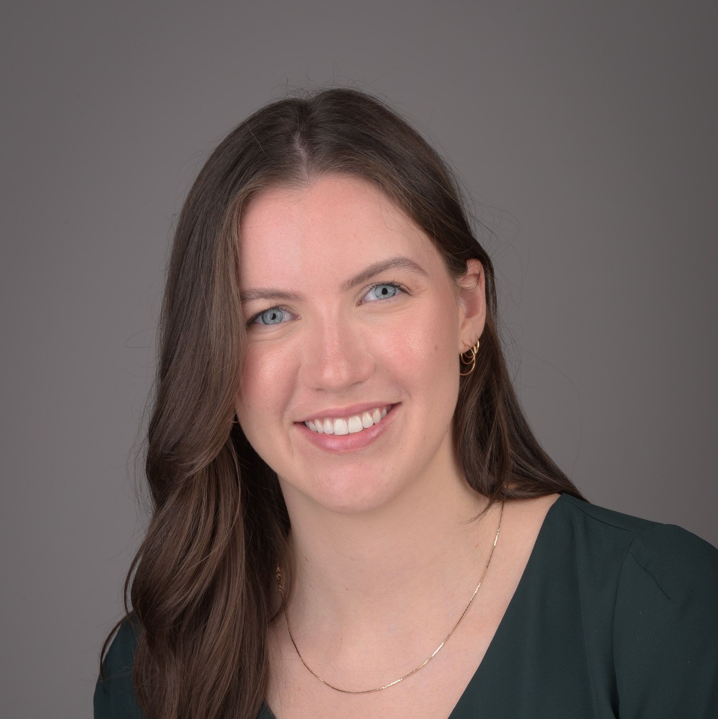 Alexandra smiling in front of a grey background.