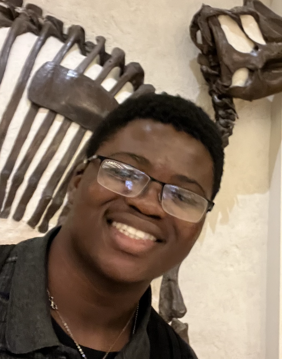 Portrait photograph of George smiling in front of dinosaur bones.