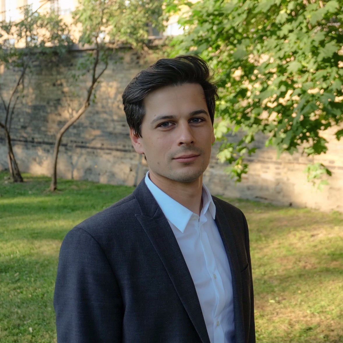 Gregoire standing in front of a stone wall and some trees. 