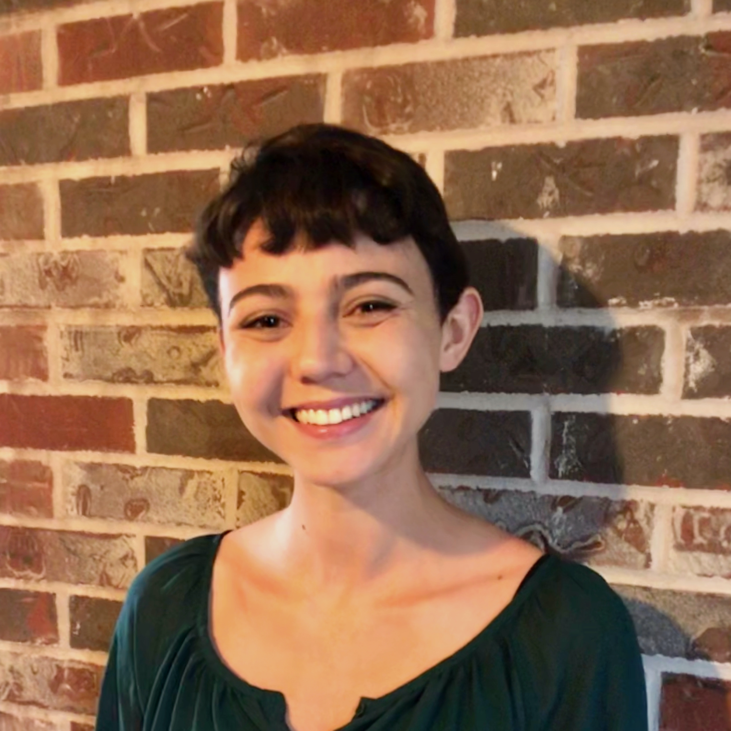 Celia smiling in front of a brick wall. 