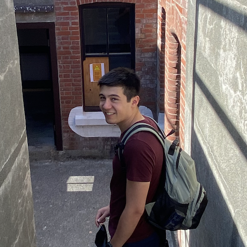 Benjamin smiling and standing on steps down to a red brick building.