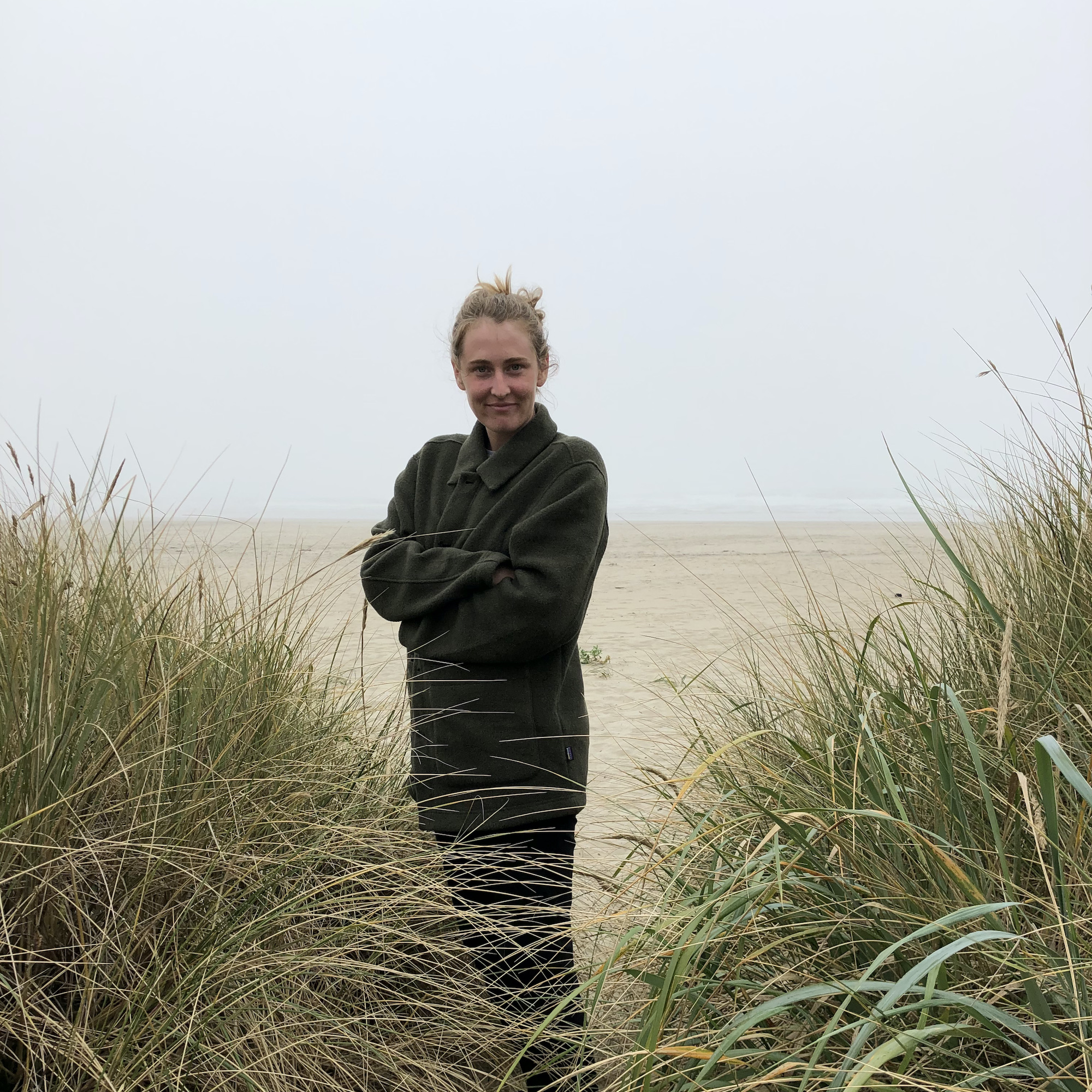Alexandra smiling and standing by some rushes by a beach. 