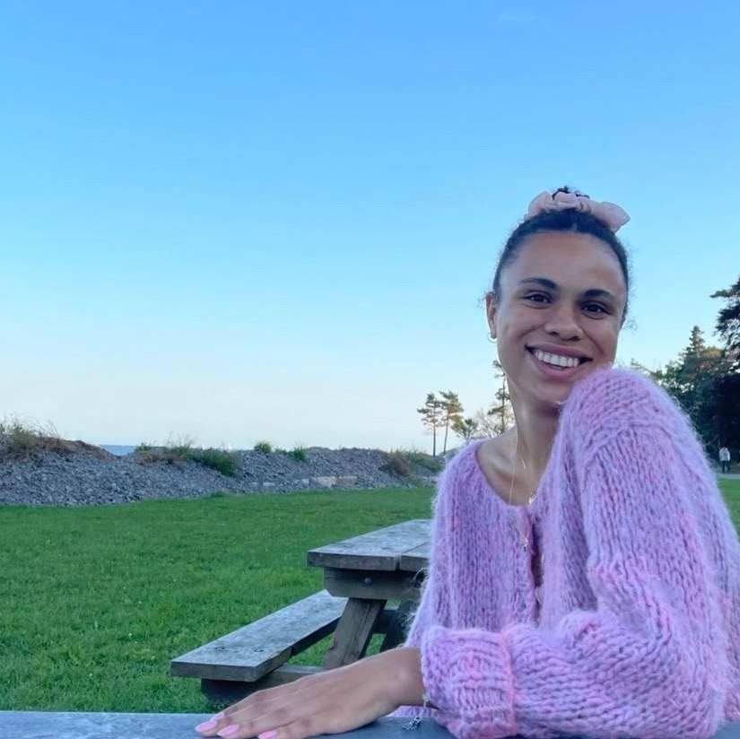 Jane smiling and sitting on a bench in front of a grassy field.