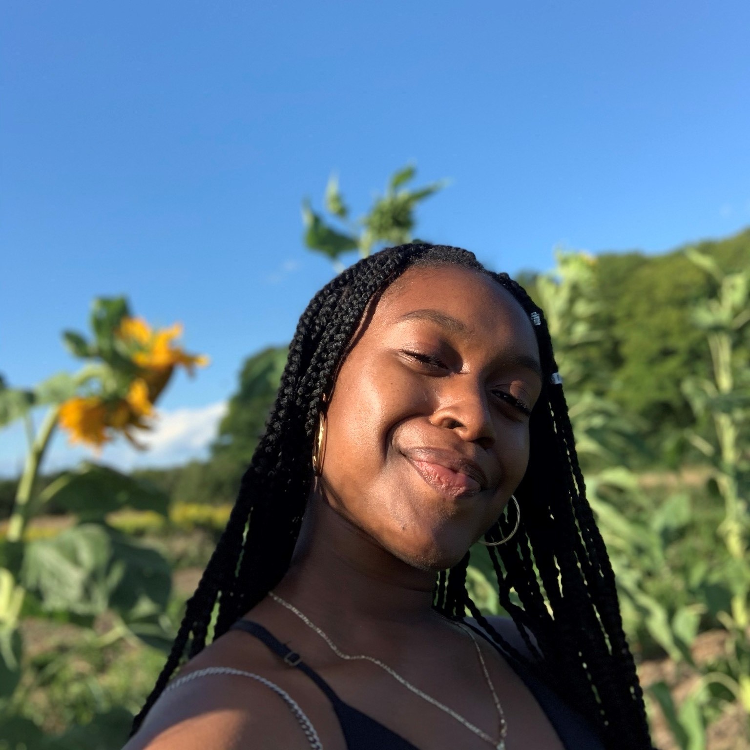 Jhamela smiling in front sunflowers. 