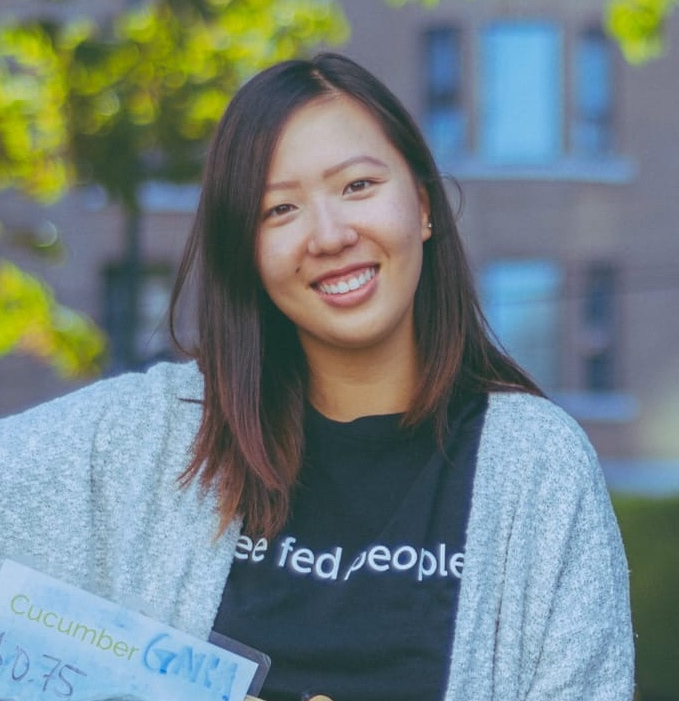 Katelyn smiling in front of a blurred background of trees and a building.