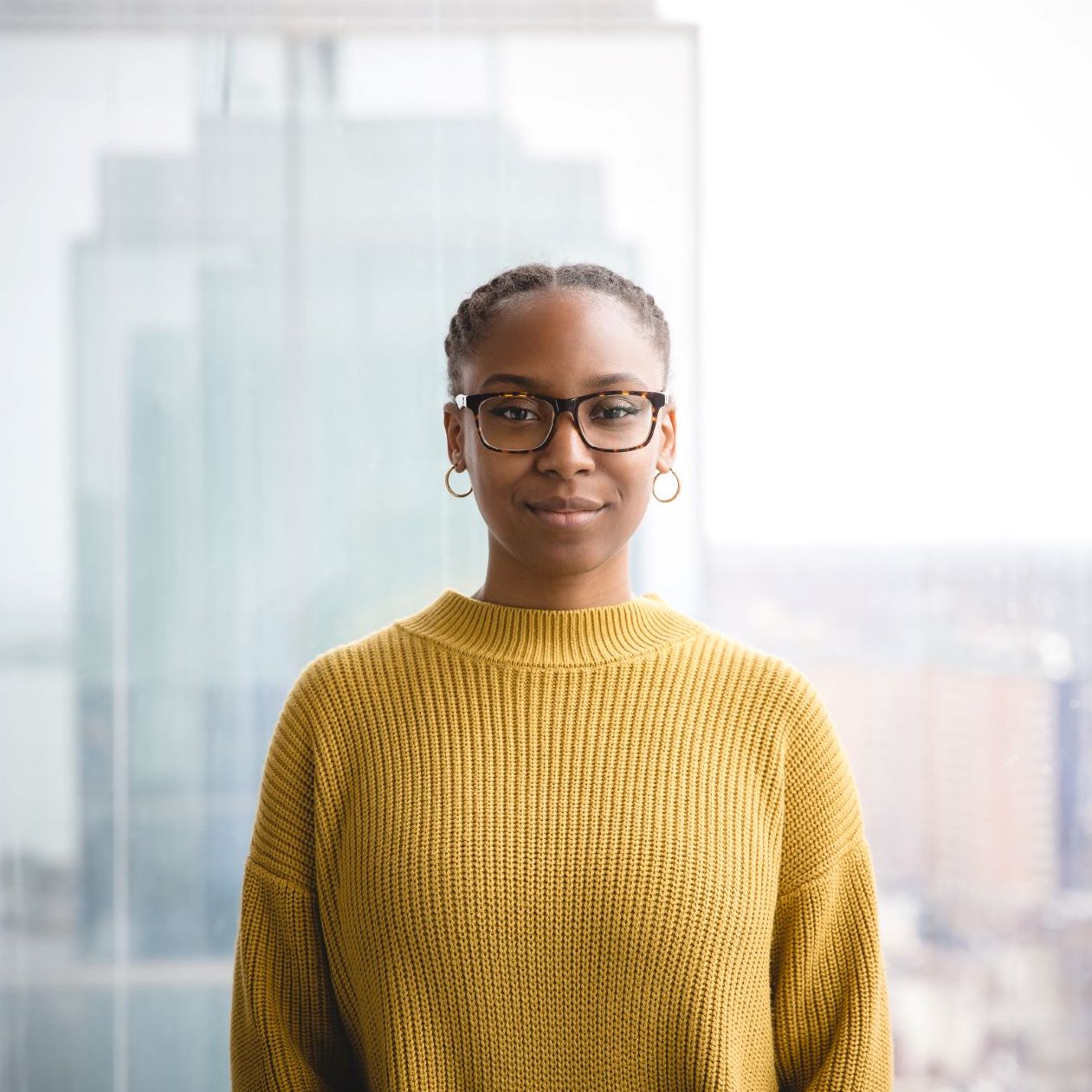 Keisha smiling in a yellow sweater in front of buildings. 