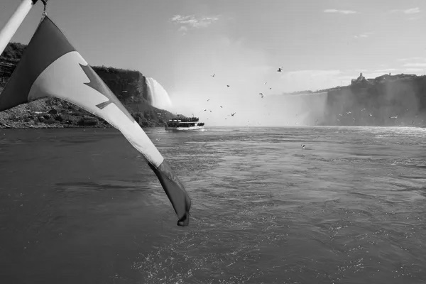 Black and white photograph of Niagara falls and the Canadian flag. 