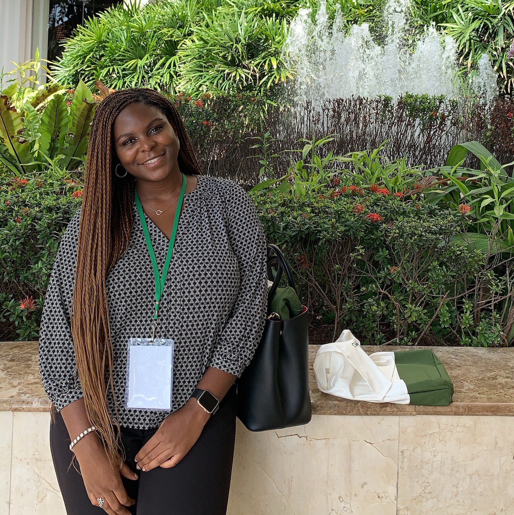 Omobolanle smiling and standing in front of a fountain and plants. 