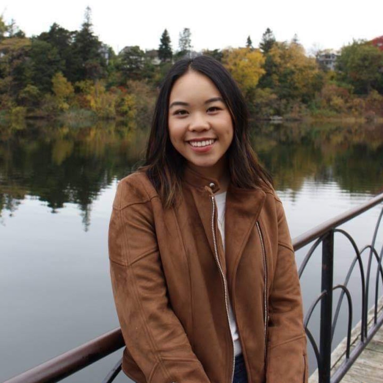 Rebecca smiling and standing in front of a body of water, surrounded by trees. 