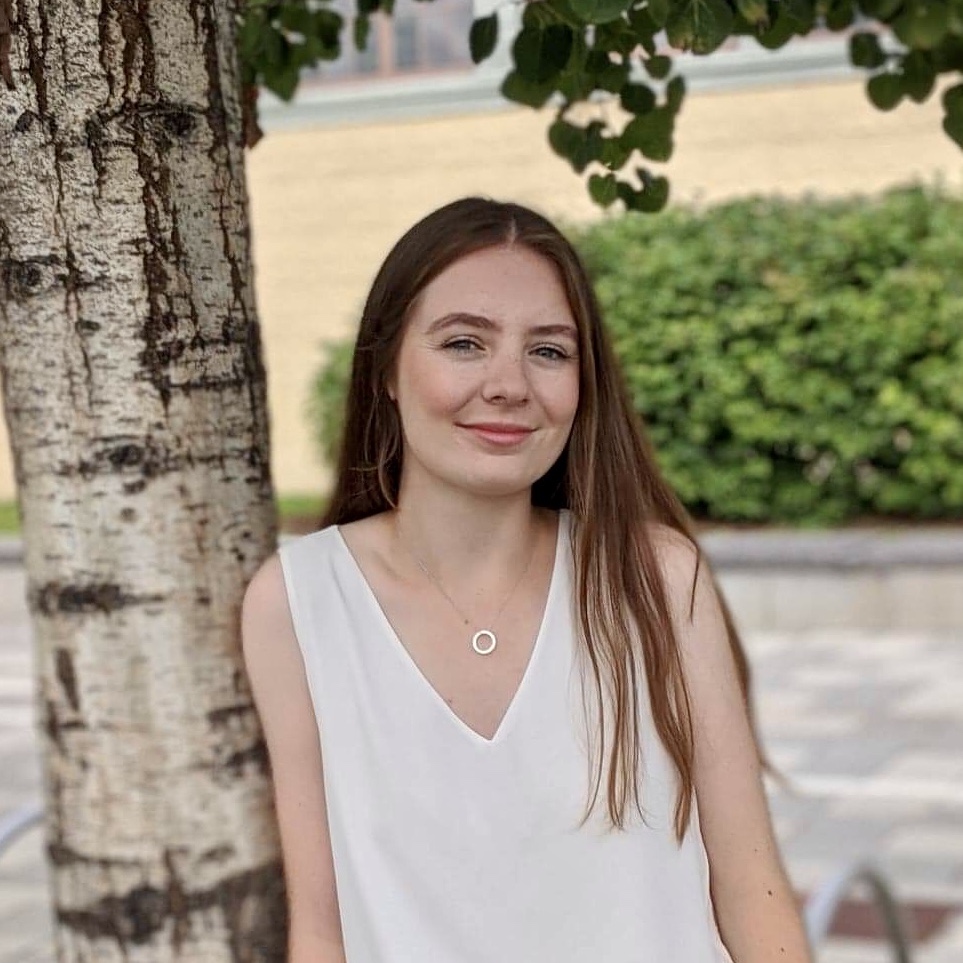 Siobhan smiling and leaning against a tree.