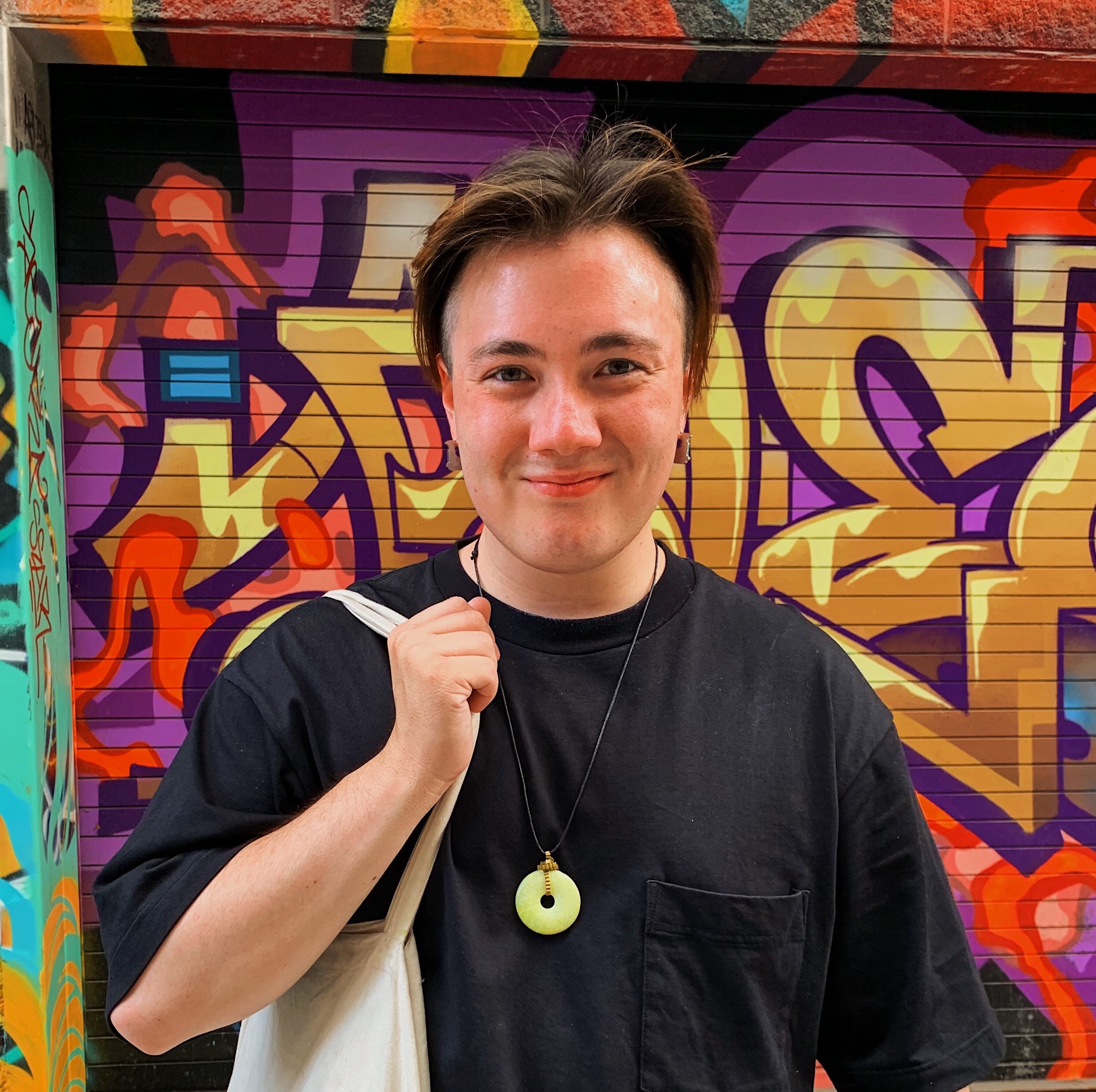 Thomas smiling and standing in front of a colourful mural.