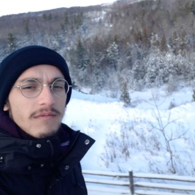 Hikmat smiling in front snowy forest. 