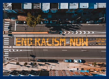 Aerial photograph of a city street. Graffiti on the street reads 'End Racism Now'