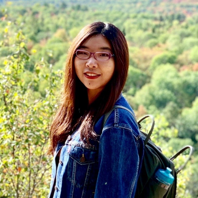 Annie smiling and standing in front of some trees.