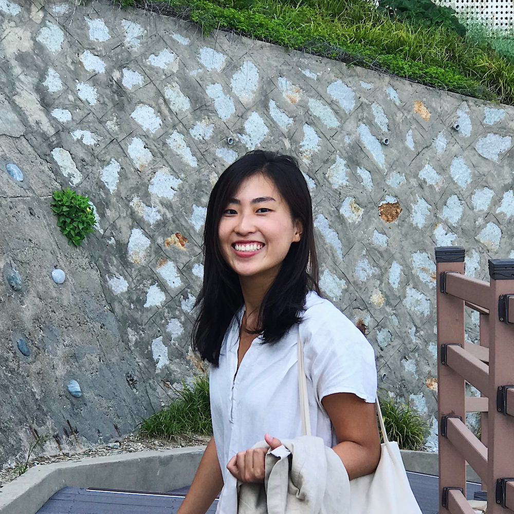 Gyoorie smiling in front of a stone wall. 