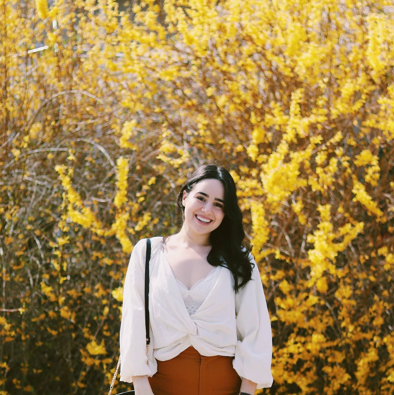 Demetra smiling and standing in a field of yellow flowers. 