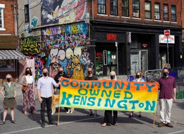 Protesters standing holding a banner that reads &amp;quot;Community Owned Kensington&amp;quot; 