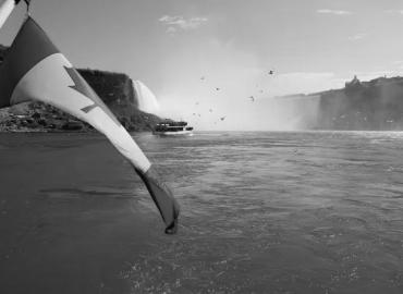 Black and white photograph of Niagara falls and the Canadian flag. 