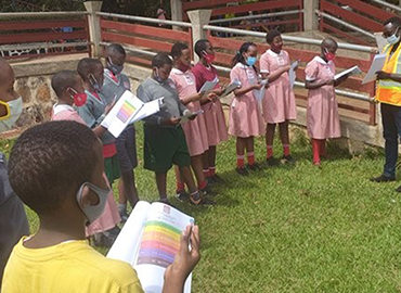 Students in Kigali, Rwanda are gathered outside with a researcher. They are all wearing medical masks and reading pamphlets.